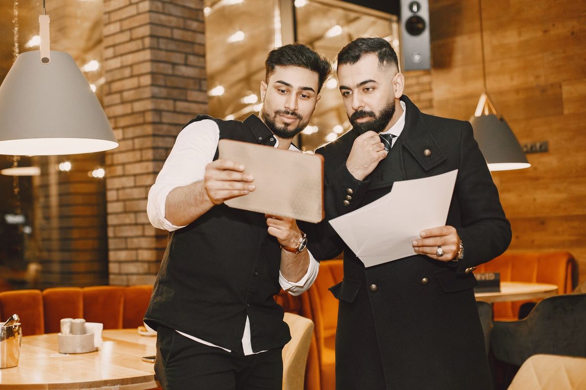 Deux responsables d'un restaurant consultent ensemble une tablette et une feuille de planning dans la salle
